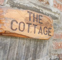 A wooden sign with the words The Cottage on a stone wall at Lower West Curry Cottage in Launceston