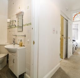 A small bathroom with a toilet and sink next to a hallway leading to a bedroom at Pier View in Paighton