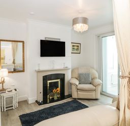 A small living room with a beige armchair a fireplace a wall-mounted TV and a side table with a lamp at Pier View in Paighton