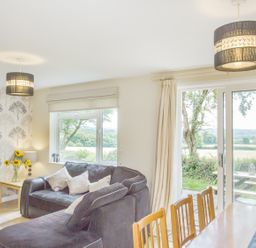 A living room with a black sofa table with sunflowers and a dining table near large windows and sliding doors at Dartmoor View in Gunnislake