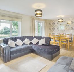 A living room with a black sectional sofa and a wooden dining table with chairs at Dartmoor View in Gunnislake