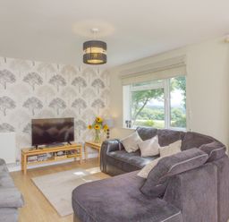 A living room with a television on a wooden stand and sofas near a window at Dartmoor View in Gunnislake