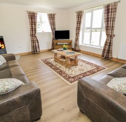 A living room with two brown sofas a coffee table a rug a wood burning stove and a television at Rede River Cottage in West Woodburn