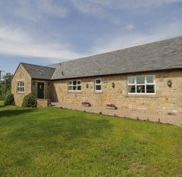 A stone cottage with a slate roof surrounded by grass and a paved driveway at Rede River Cottage in West Woodburn