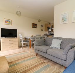 A living room with a gray sofa a television on a dresser and a dining table with chairs at 104 Sunrise Drive in Filey