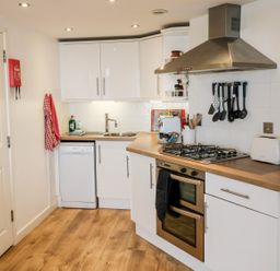 A kitchen with white cabinets wooden countertop a gas stove oven sink dishwasher and various utensils at 10 Oceanside in Ilfracombe