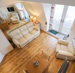 A living room with white leather sofas a wooden dining table and chairs wooden flooring and glass doors at 10 Oceanside in Ilfracombe