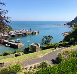 A coastal bay with boats docked near a pier and a pathway with greenery overlooking the sea at 10 Oceanside in Ilfracombe