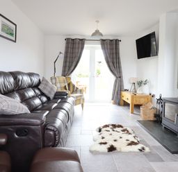 A living room with a leather sofa armchair wood stove and TV at Gwynfa in Rhyd Uchaf near Bala Gwynedd