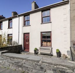 A white terraced house with red doors and windows and a stone wall in front at Miners Cottage in Blaenau Ffestiniog