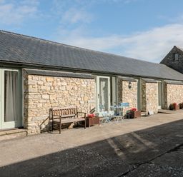 A stone building with light green doors brown bench blue table and chairs and flower pots outside at Snowdrop Cottage in Llantwit Major