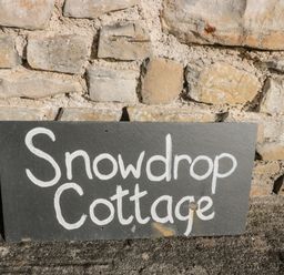 A stone wall with a black rectangular sign reading Snowdrop Cottage in white letters at Snowdrop Cottage in Llantwit Major