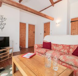 A living room with a floral sofa red cushions wooden beams three wooden doors and a wooden coffee table with glassware at Snowdrop Cottage in Llantwit Major