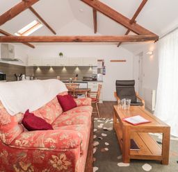 A living area with red floral sofa, wooden coffee table, black armchair, dining table, and kitchen cabinets at Snowdrop Cottage in Llantwit Major