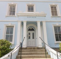 The front entrance of a blue building with white columns and steps with plants on either side at Bank House