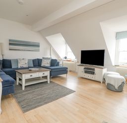 A living room with a large blue sectional sofa cushions coffee table television and windows at Dawn Catcher in Falmouth