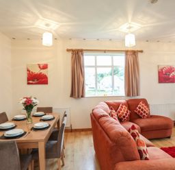 A living room with an orange sofa and a dining table set with plates and flowers at The Cabin in Combe Martin