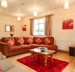 A living room with an orange sofa red cushions wooden coffee table and a television at The Cabin in Combe Martin