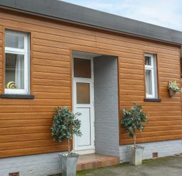 An exterior view of a building with wooden siding two windows a door and potted plants at The Cabin in Combe Martin