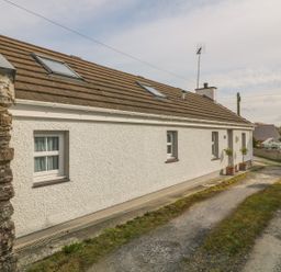 Exterior view of a white single-story house with a tiled roof and skylights along a gravel driveway at Tyn Y Giat Brynsiencyn near Beaumaris