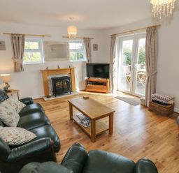 A living room with green leather sofas a fireplace a wooden coffee table a television and glass doors leading outside at Tyn Y Giat in Brynsiencyn near Beaumaris