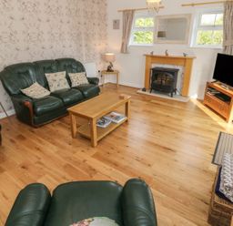 A living room with green leather sofas a wooden coffee table a fireplace and a television at Tyn Y Giat in Brynsiencyn near Beaumaris