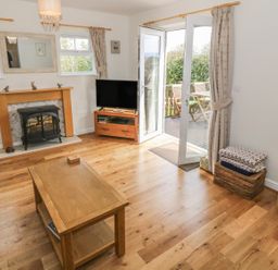 A living room with a wooden coffee table a fireplace and a television near open double doors leading to an outdoor patio at Tyn Y Giat in Brynsiencyn near Beaumaris