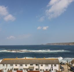A row of houses by the ocean with waves and a cliff in the background at Sennen Heights in Sennen Cove near Penzance
