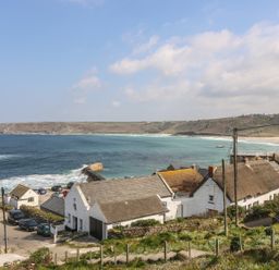 A coastal village overlooking the sea with houses and cars near a beach at Sennen Heights in Sennen Cove near Penzance