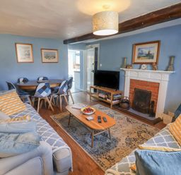 A living room with a sofa, dining table and television at Delphinium in Blakeney, Norfolk