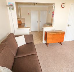 A brown sofa with white pillows next to a wooden drop leaf table and a kitchen area in the background at Surf in Hunstanton