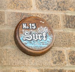 A round wooden sign with number 15 and word Surf attached to a stone wall at Surf in Hunstanton