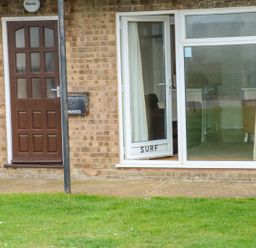 A brick exterior of a building with a brown door and a white patio door labeled Surf at Surf in Hunstanton
