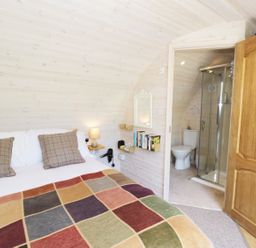 A bedroom with a bed pillows bedside lamp bookshelves and an open door showing a bathroom with a toilet and shower at Idris Pod in St Asaph