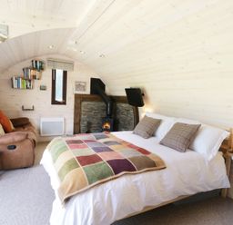 A curved wooden room with a bed a sofa a fireplace and a small television at Idris Pod in St Asaph