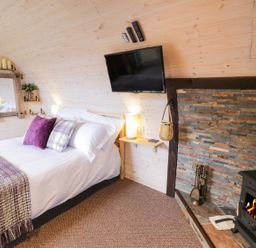 A bedroom with a bed pillows and blanket a wall-mounted television and a fireplace with fire at Gelert Pod in St Asaph