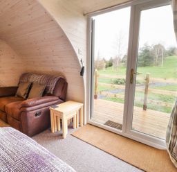 A brown leather armchair with side tables next to sliding glass doors showing a green garden outside at Gelert Pod in St Asaph