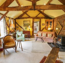 A living room with exposed wooden beams a fireplace and various chairs at Dolgenau Hir - The Barn in Llawr y Glyn near Trefeglwys