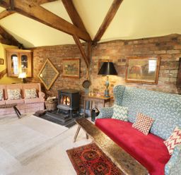 A living room with two sofas a wood stove and wooden beams on the ceiling at Dolgenau Hir - The Barn in Llawr y Glyn near Trefeglwys