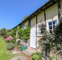 Exterior of a house with white windows and door surrounded by green plants and flowers at Dolgenau Hir - The Barn in Llawr y Glyn near Trefeglwys