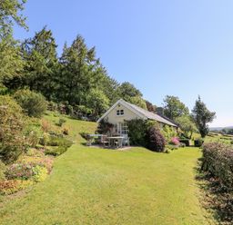 A small house with outdoor furniture on a lawn surrounded by trees and plants at Dolgenau Hir - The Barn in Llawr y Glyn near Trefeglwys