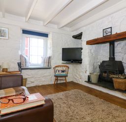 A living room with a stone fireplace a television a wooden chair and a sofa at Ner Sea in Marazion