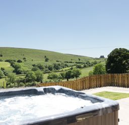 An outdoor hot tub on a patio overlooking green hills and trees at 1 Beacon View Barn in Beguildy near Knighton