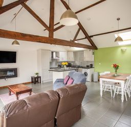 An open living area with wooden beams a kitchen dining table with flowers and a sitting area at 1 Beacon View Barn in Beguildy near Knighton