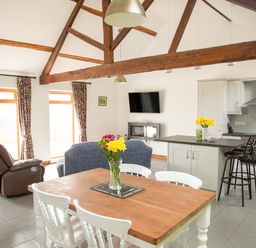 A kitchen dining and living area with wooden beams wooden dining table white chairs and a wall mounted TV at 1 Beacon View Barn Beguildy near Knighton