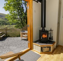 A wood burning stove near an open door leading to an outdoor area with a picnic table and hot tub at Moelfre - Shepherds Hut in Llanbedr