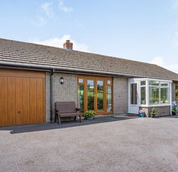 A single story brick house with a wooden garage door wooden framed glass doors a small porch and outdoor seating at Yr Hen Ffald in Pontarddulais