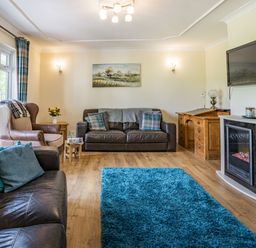 A living room with leather sofas a blue rug a wooden desk and a wall-mounted television at Yr Hen Ffald in Pontarddulais
