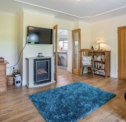 A living room with a blue rug a wall mounted tv a fireplace wooden furniture and an open door at Yr Hen Ffald in Pontarddulais