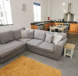 An open living room and kitchen with a gray sectional sofa and wooden cabinets at The Shell at the Hideaway in Tenby